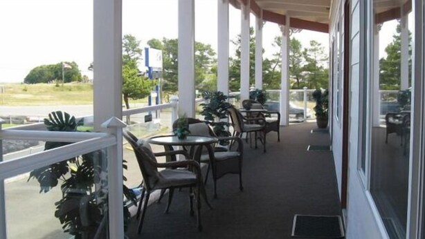A covered outdoor seating area with tables and chairs, large windows, and potted plants. - Breakers Boutique Inn (Westport)