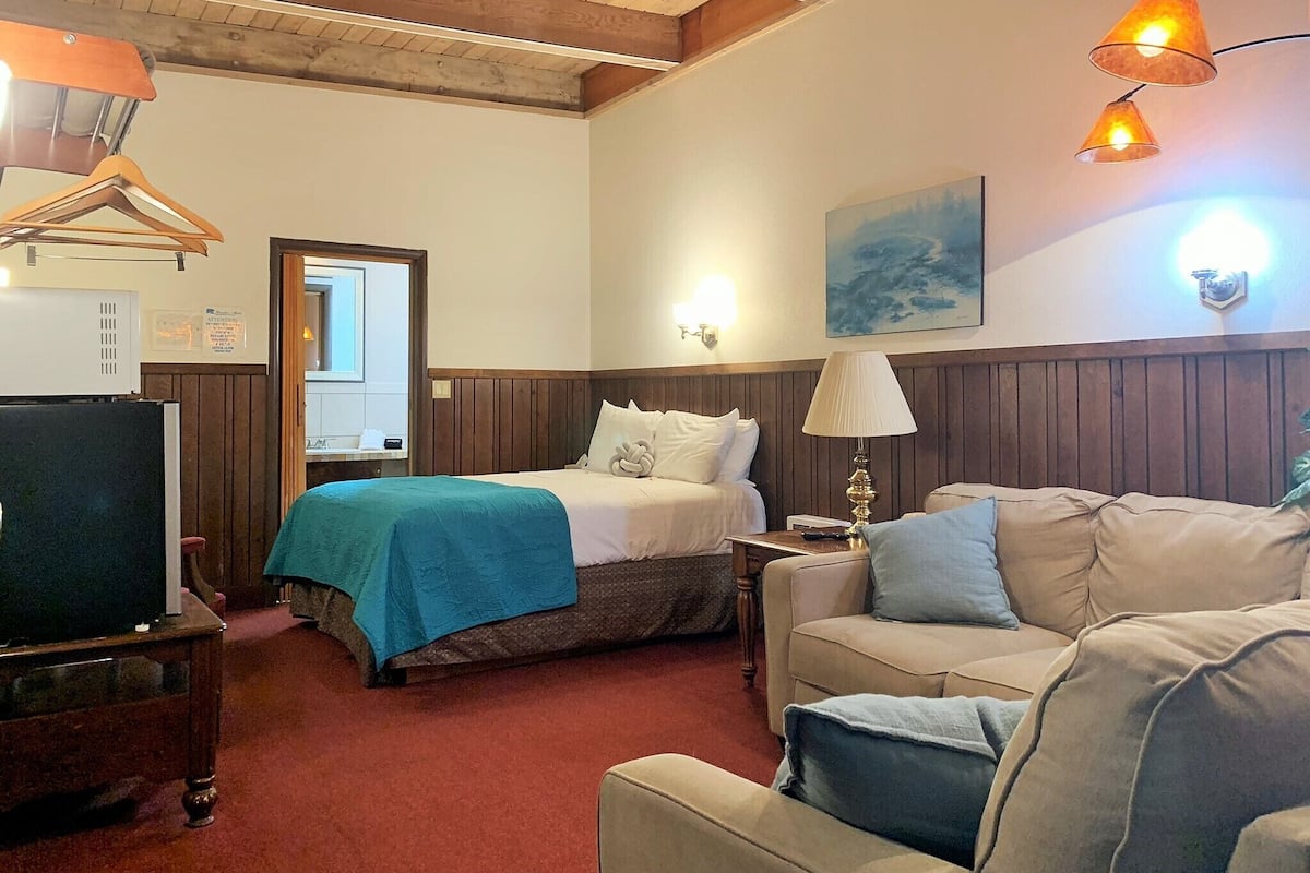 A hotel room with a bed, a sofa, a TV, and a lamp.