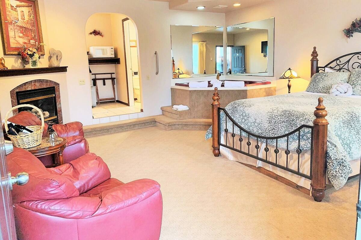 A bedroom with a bed, a chair, a mirror, and a fireplace.