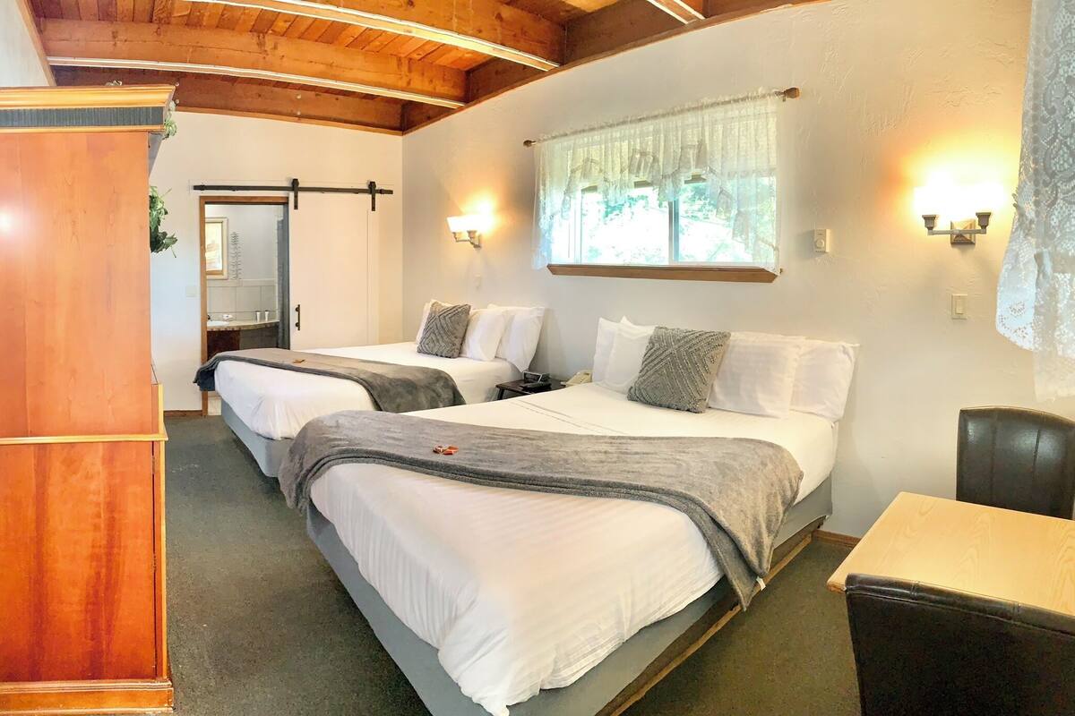 A hotel room with two beds, a wooden wardrobe, a window with lace curtains, and a small table.