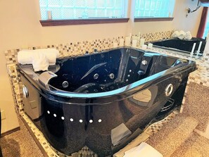 A modern bathroom with a black jacuzzi tub, a tiled shower area, and a window with a view of the outside. - Breakers Boutique Inn (Westport)