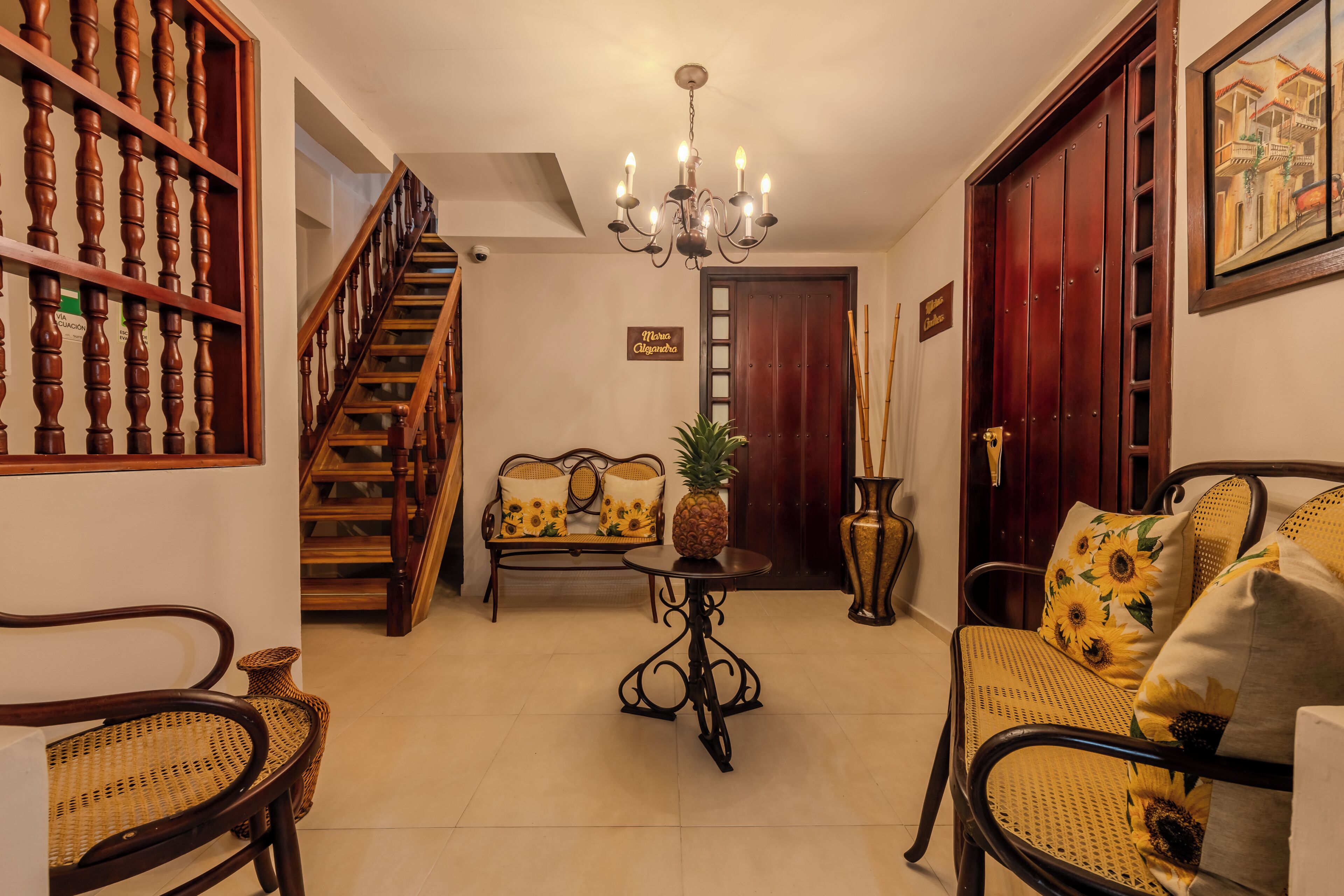 Una sala de estar con una escalera, una araña, muebles de mimbre y una puerta con un letrero.