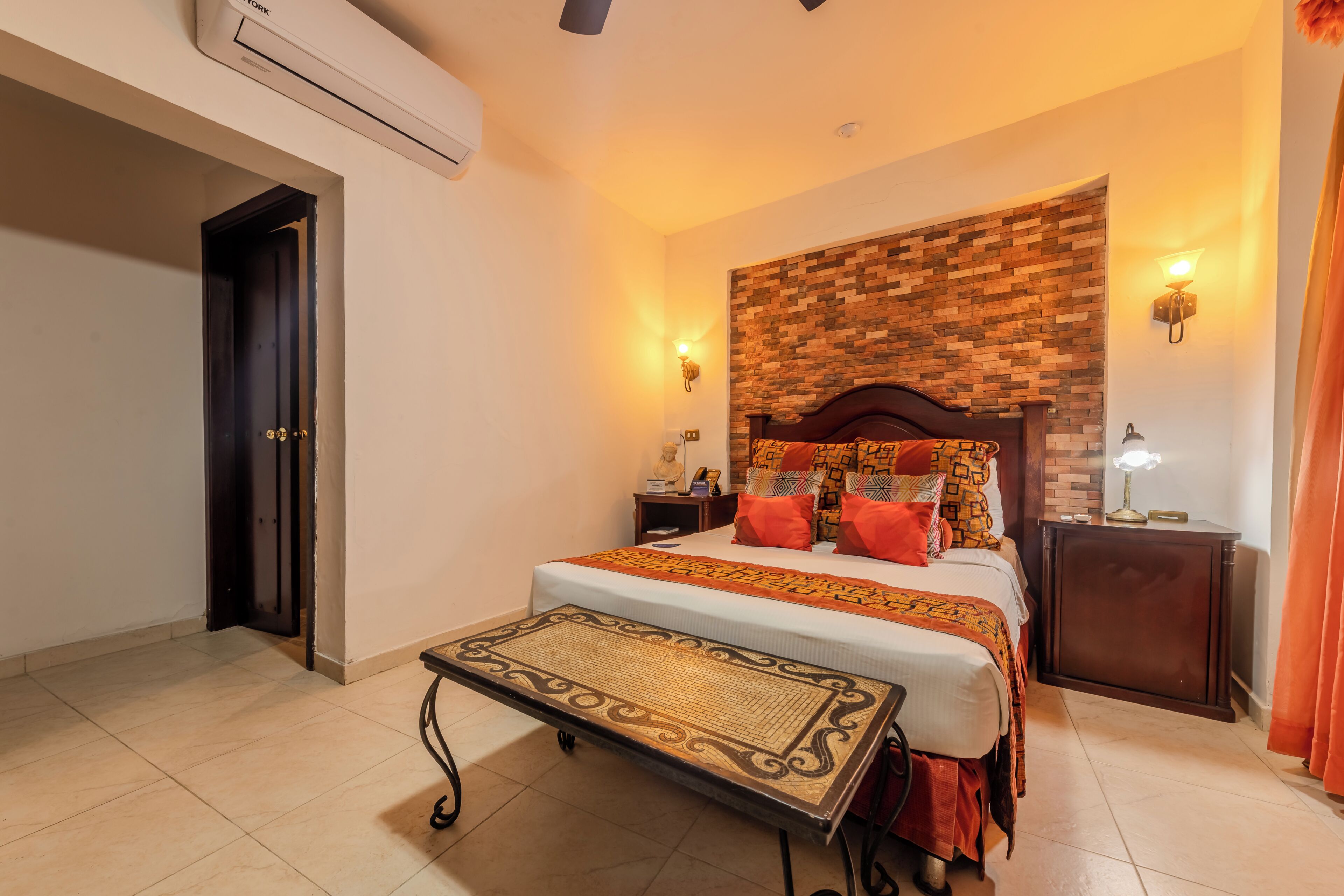 A hotel room with a bed, bedside tables, a wall-mounted air conditioner, and a door.