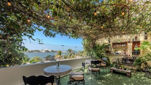 Un balcón con vistas al mar, mobiliario exterior y una zona de bar con plantas y botellas.