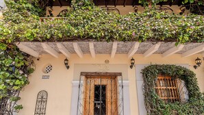 Fachada de edificio con una reja de hierro forjado, una puerta de madera y un balcón cubierto de follaje.