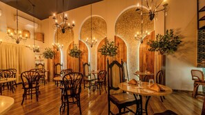 Un interior de restaurante con mesas y sillas de madera, candelabros colgantes y plantas decorativas.