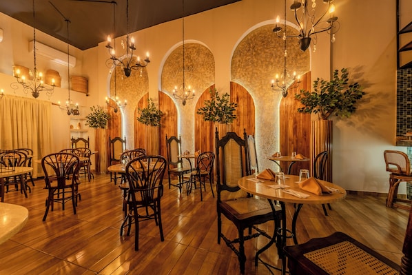 Ein Restaurantinneres mit Holztischen und -stühlen, hängenden Kronleuchtern und Zierpflanzen.