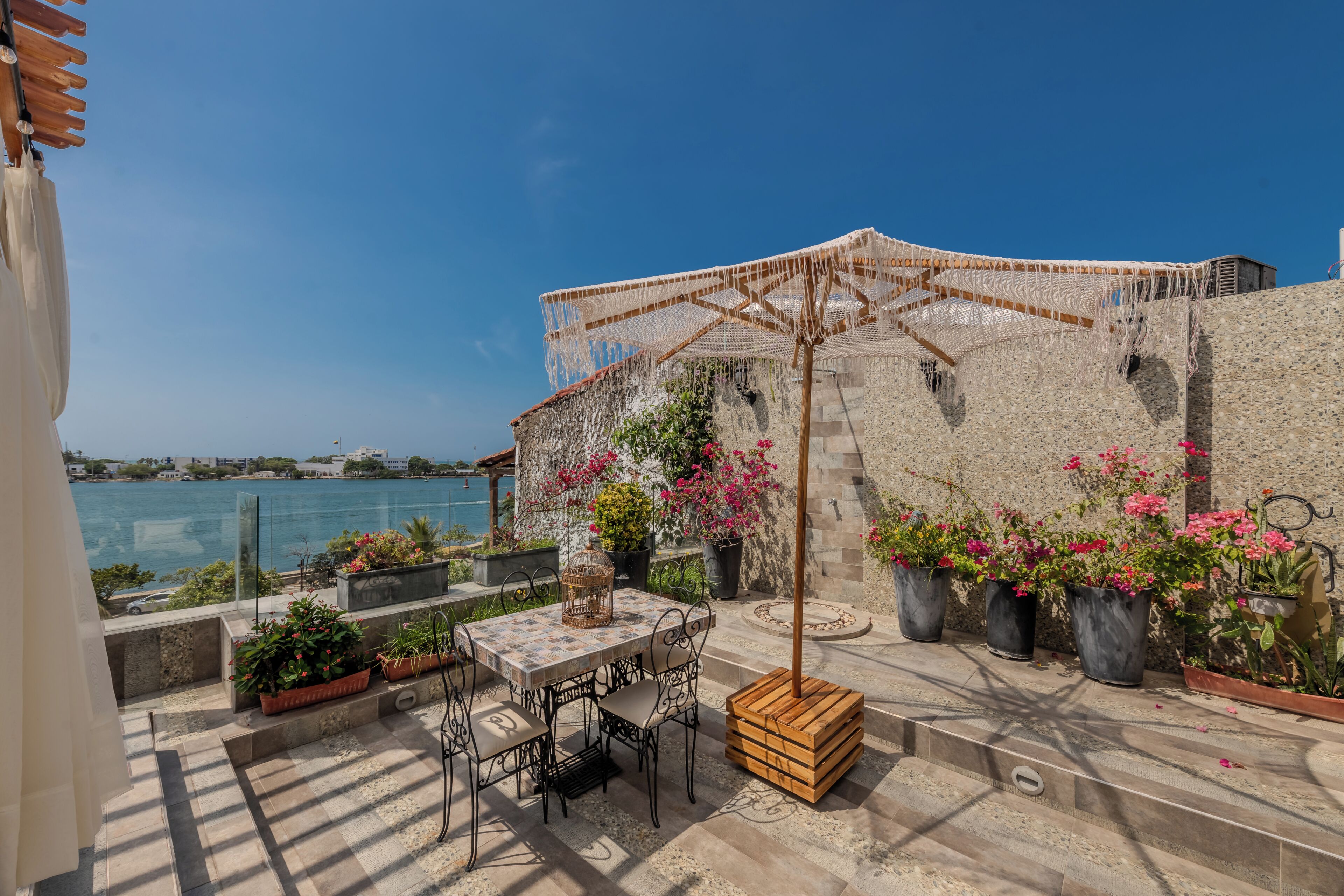 A rooftop terrace with a table and chairs, potted plants, and a view of the sea.