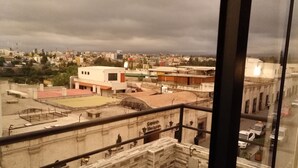 Uma varanda com vista para a paisagem urbana, incluindo um restaurante chamado "Il Romano" e um edifício com uma placa "Phoenix".