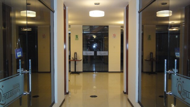 Corredor de hotel com portas de vidro, balcão de recepção e placa indicando área proibida para fumantes.