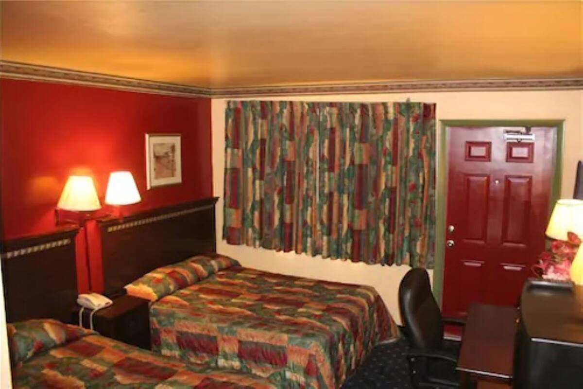 A hotel room with two beds, a desk, a chair, a telephone, and a door.