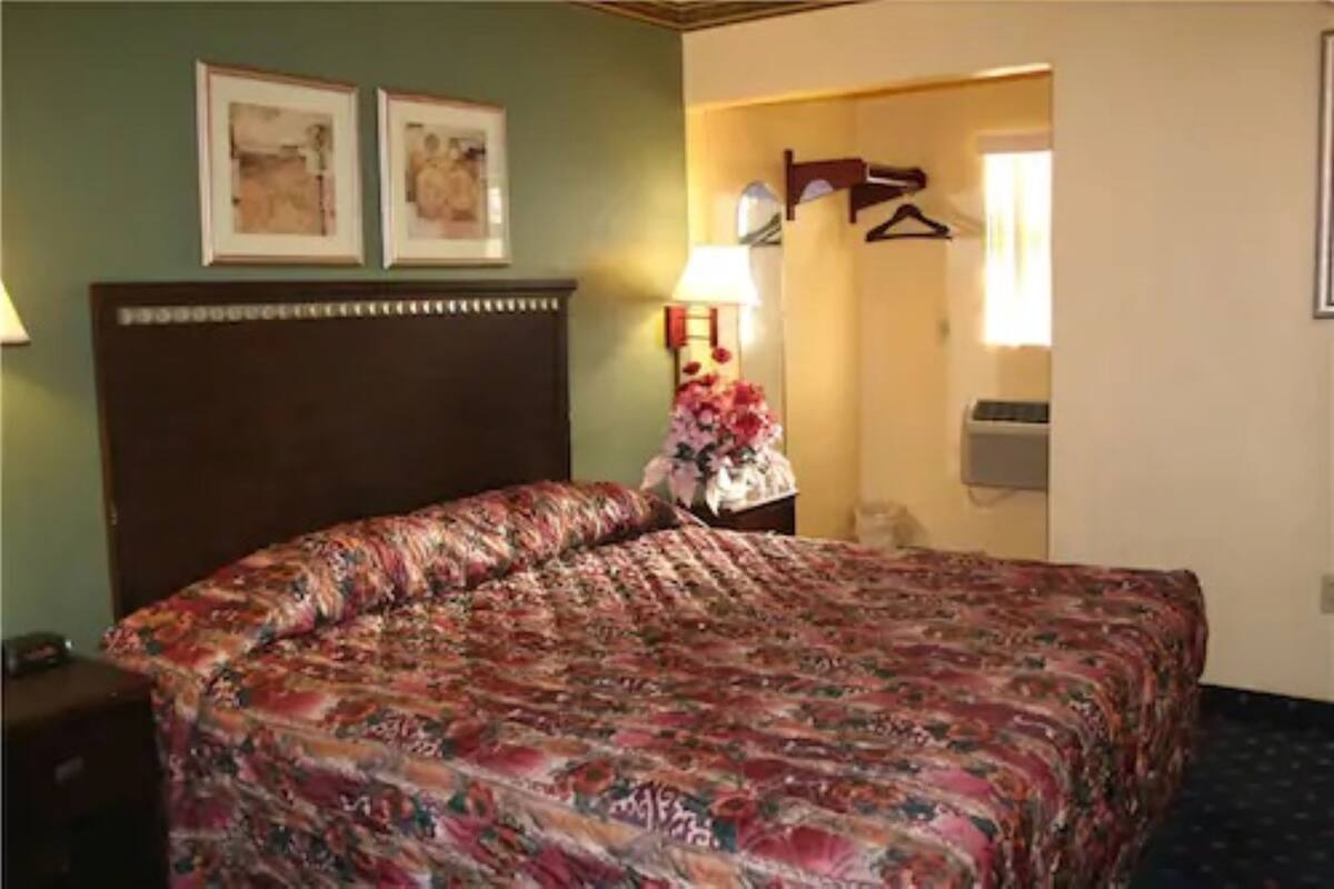 A hotel room with a large bed, a nightstand, a lamp, and a door leading to a bathroom.