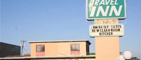 Un panneau indiquant un « Travel Inn » avec une affiche « Pas de distributeurs automatiques », un panneau indiquant une « Nouvelle cuisine dans les chambres », et un bâtiment avec une porte et des fenêtres rouges.