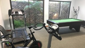 A room with a stationary bike, a pool table, and a brick wall with a window.