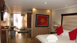 A hotel room with a large bed, a small seating area, a bathroom, and a view of the outdoors.