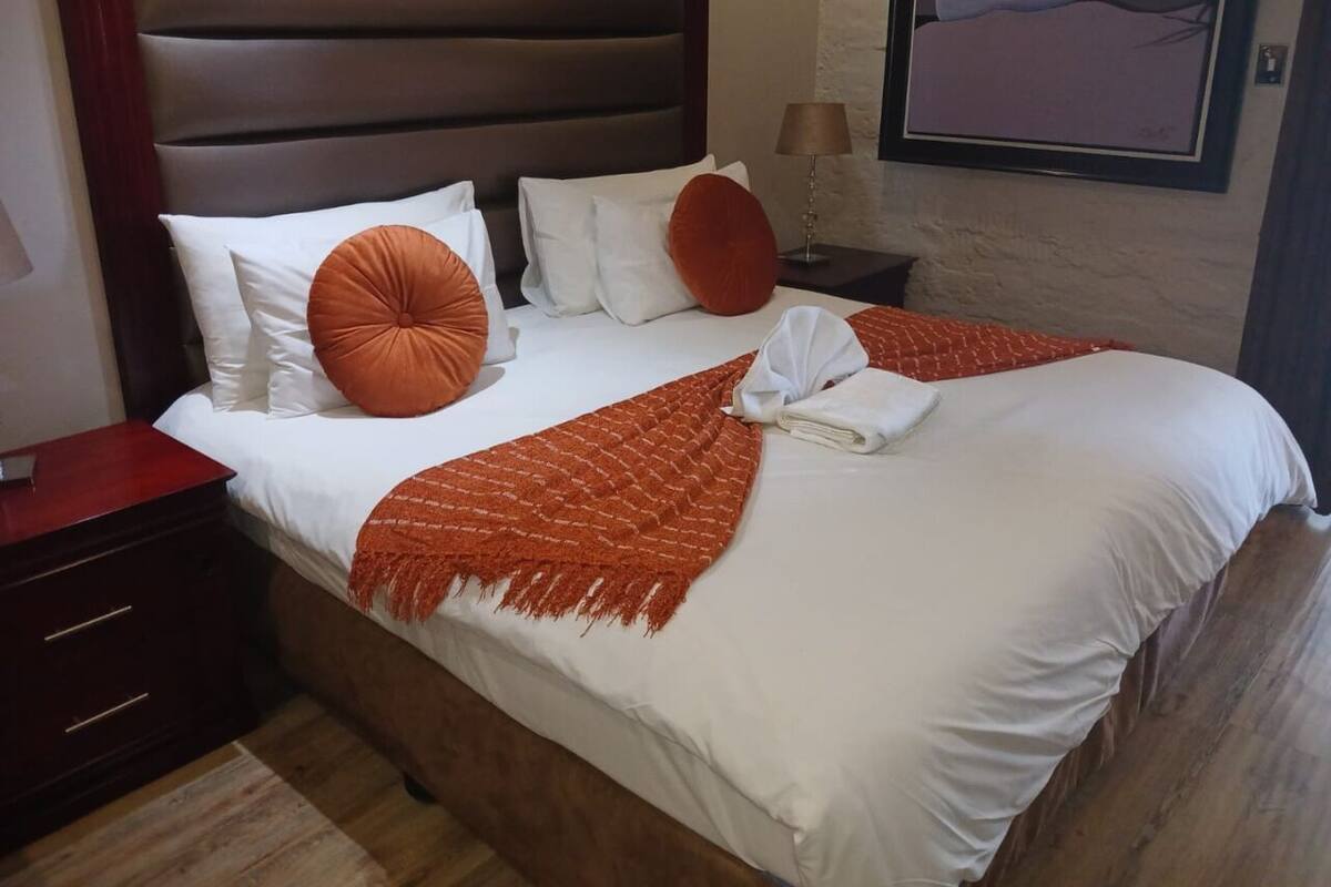 A neatly made bed with white linens, a brown headboard, and a red throw blanket.