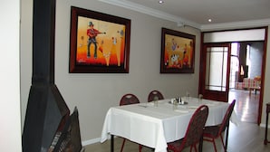 A dining area with a table set for four, chairs, a fireplace, and two paintings on the wall.