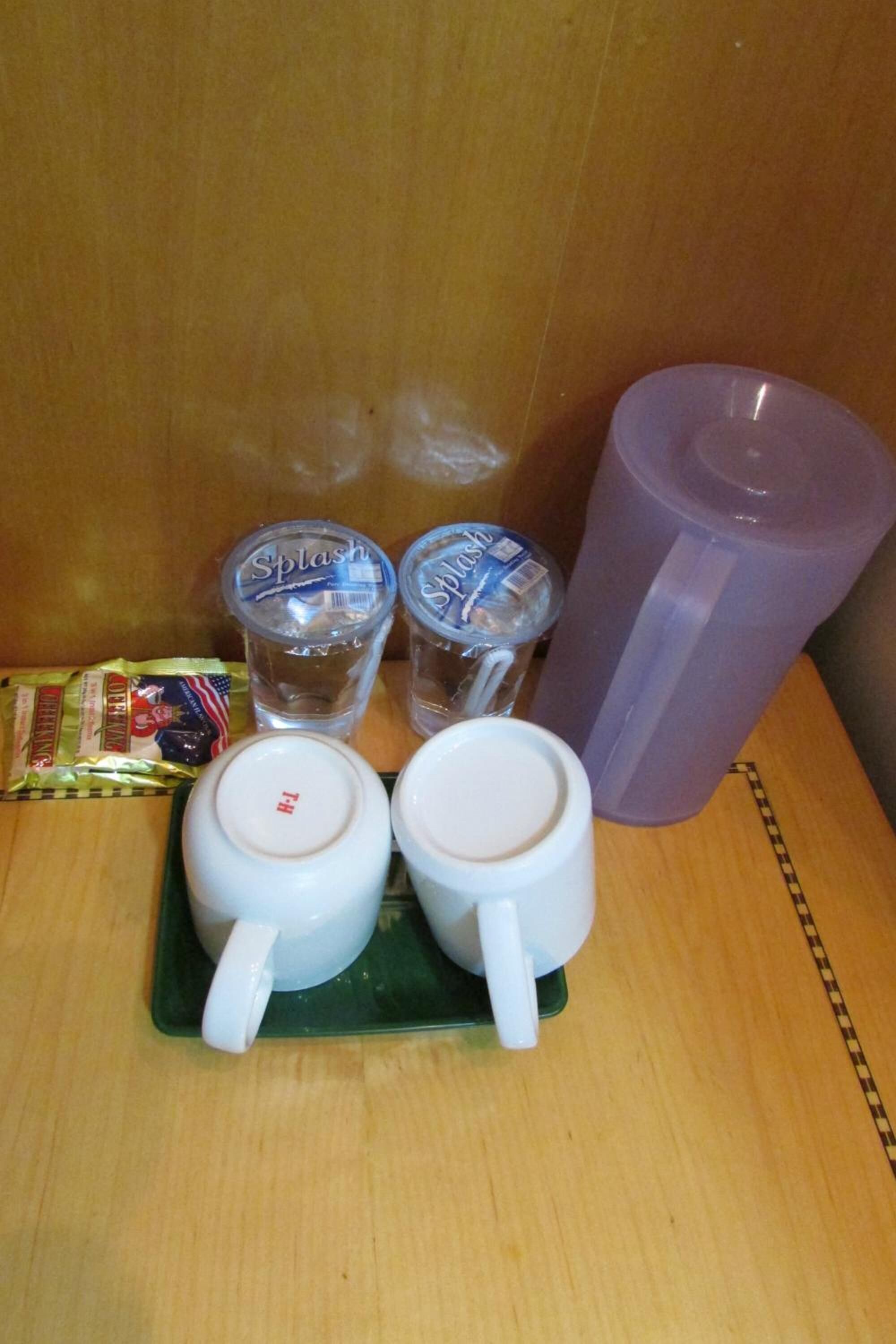 A wooden table with two white mugs, two clear plastic cups labeled 'Splash', a purple plastic cup, and a packet of snacks.