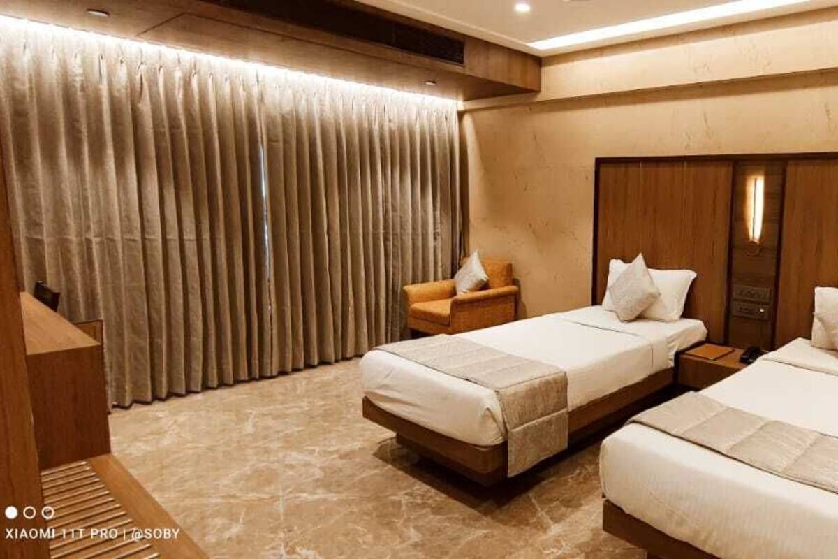 A hotel room with two beds, a wooden headboard, a chair, and a curtain.