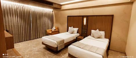 A hotel room with two beds, a wooden headboard, a chair, and a curtain.