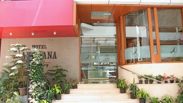 Entrada de hotel con toldo rojo, una escalera y plantas en macetas.