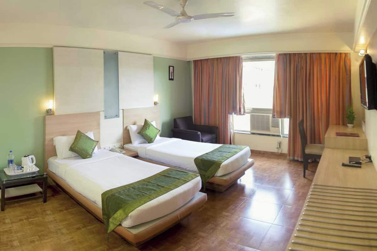 A hotel room with two beds, a desk, a chair, a TV, and a window with curtains.