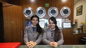 Dos recepcionistas en un mostrador, con relojes en la pared y diplomas detrás.
