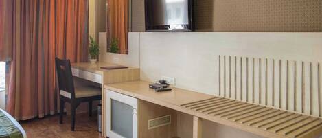 Habitación de hotel compacta con escritorio de madera, un refrigerador pequeño, un televisor sobre el escritorio y una ventana con cortinas.