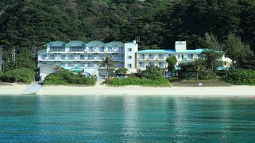 Un hotel frente a la playa con varios balcones, piscina y acceso a la playa mediante rampa.