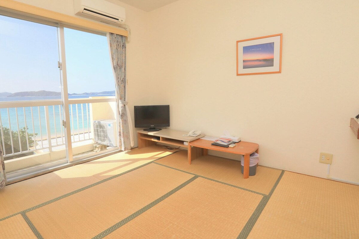 A room with a sliding glass door to a balcony, a television, a small table, and a framed picture on the wall.