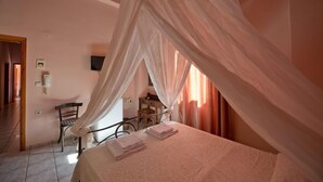 A bedroom with a bed covered by a canopy, a chair, and a bedside table with a lamp.