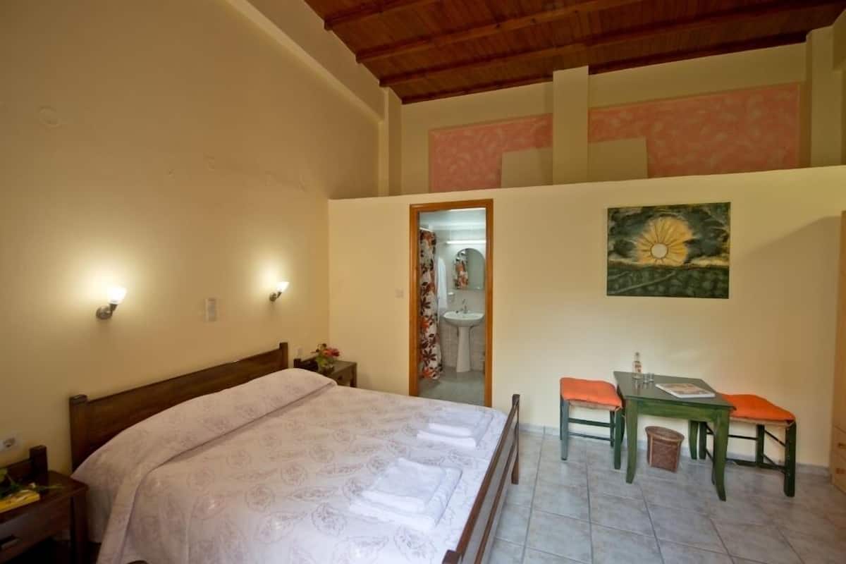 Een slaapkamer met een bed, een tafel met twee stoelen, een schilderij aan de muur en een badkamer zichtbaar door een open deur.
