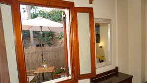 A room with a wooden desk, a mirror, and a window with an open view of an outdoor patio area.