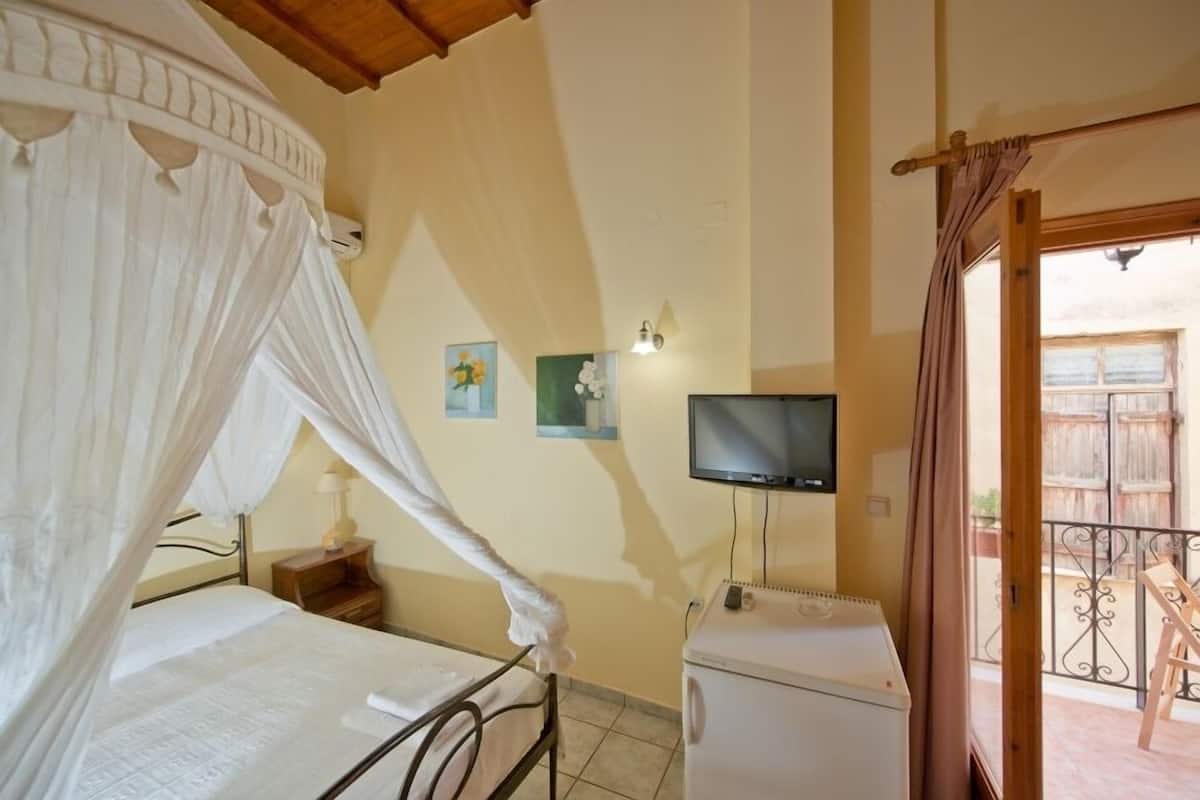 Een slaapkamer met een bed onder een baldakijn, een televisie aan de muur, en een klein wit apparaat.