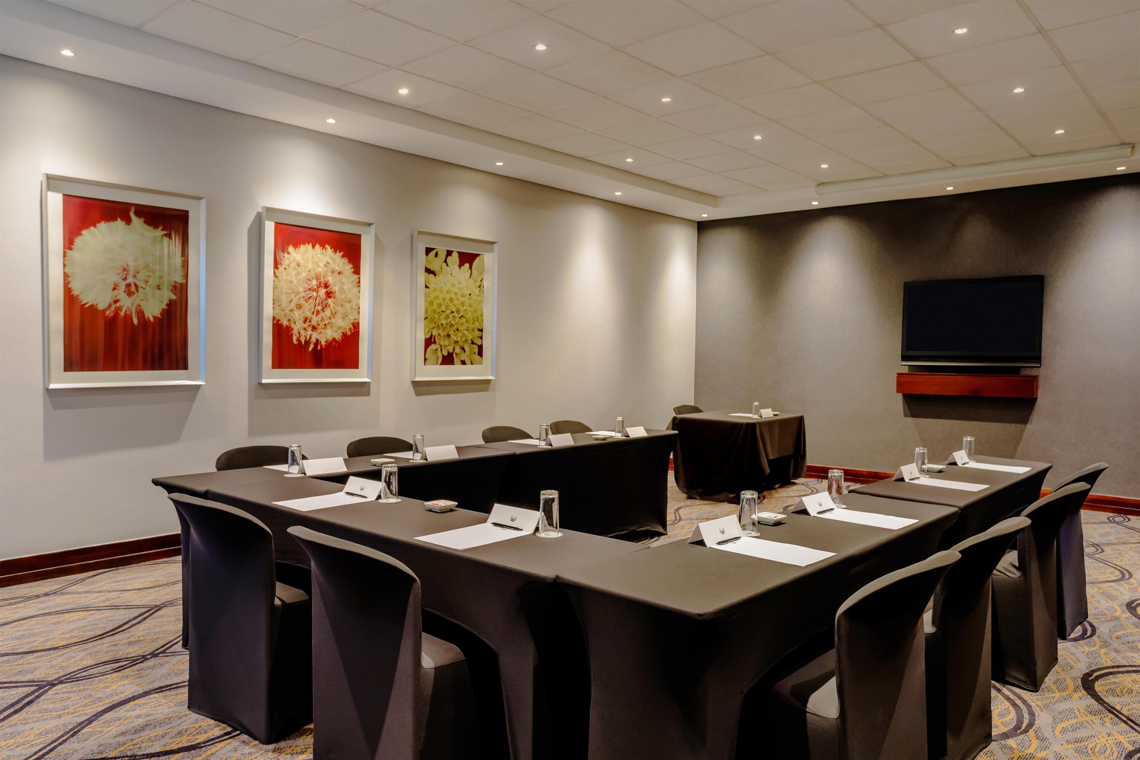 A conference room with a long table, chairs, nameplates, water bottles, and a television on the wall.