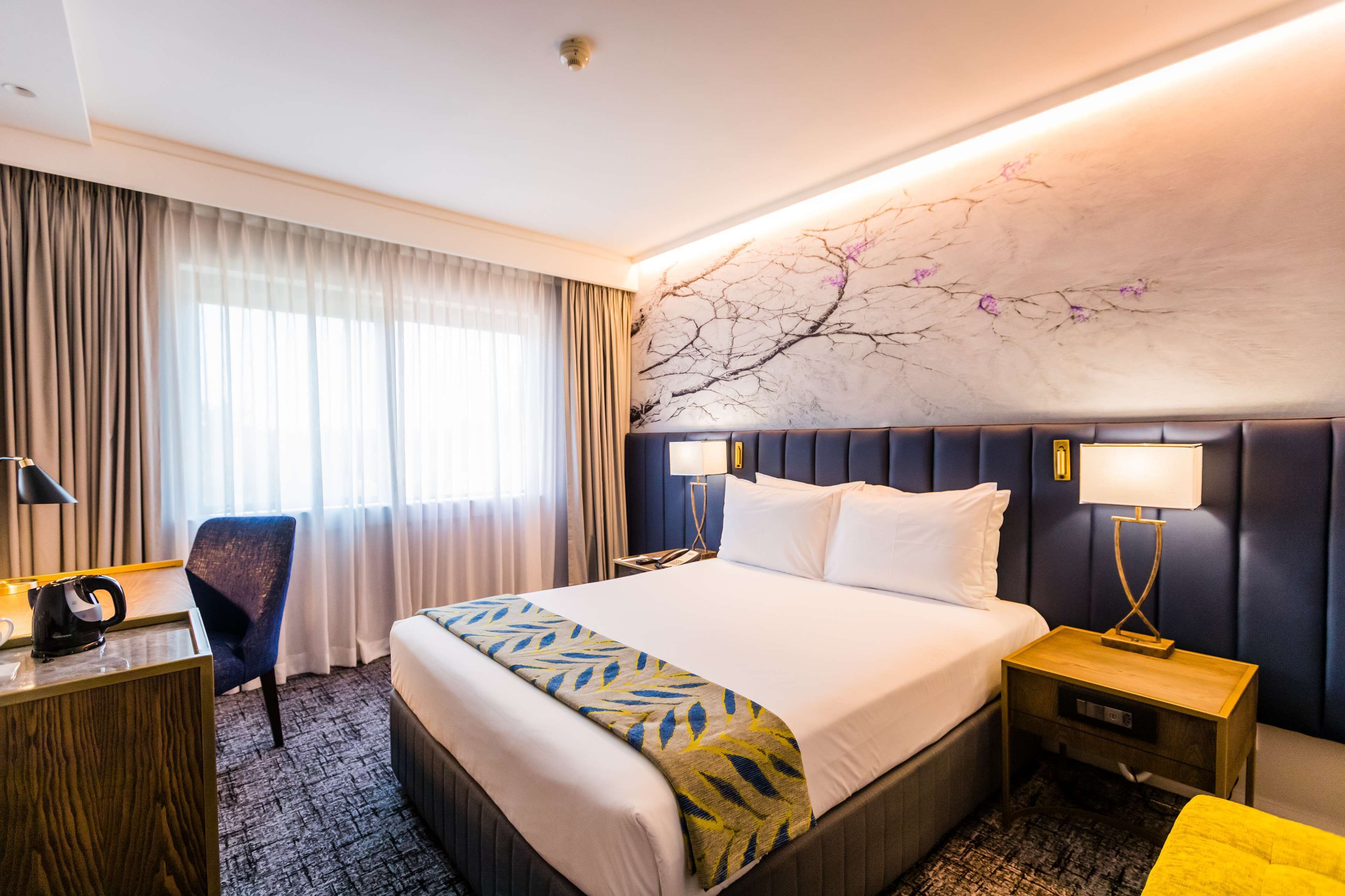 Una camera d'albergo con un letto grande, una scrivania, una sedia e un comodino con lampade.
