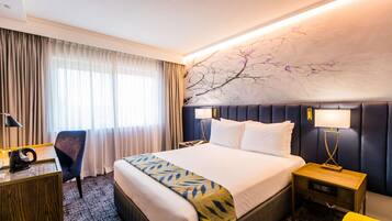 Una camera d'albergo con un letto grande, una scrivania, una sedia e un comodino con lampade.