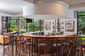 Un área de bar moderna con un mostrador curvo, diversas opciones de asientos y vista al jardín exterior.