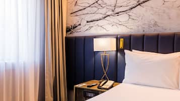Habitación de hotel con una cama grande, una mesita de noche con lámpara y una pared con un mural de una rama de árbol.