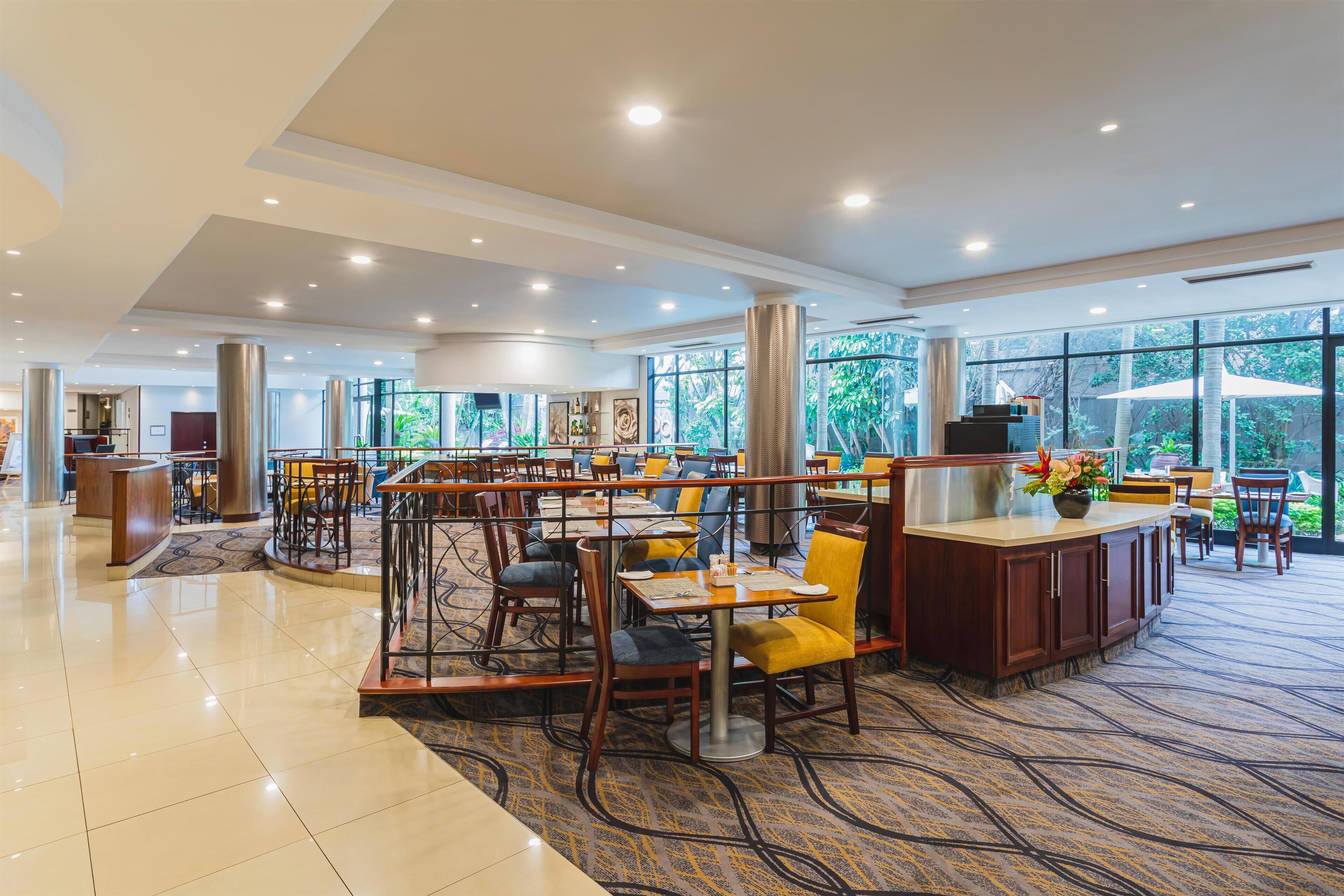 A spacious indoor area with multiple seating arrangements, a reception desk, and large windows offering a view of the outdoors.