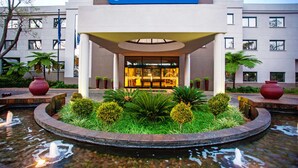 Entrada de hotel con un letrero que dice "Garden Court", rodeada por un jardín ajardinado y una fuente circular.