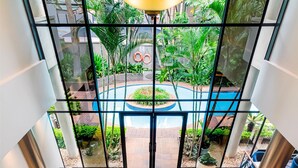 Un vestíbulo amplio con un gran muro de vidrio que ofrece vistas a una piscina y zonas verdes. Hay varias áreas de descanso con mobiliario moderno.