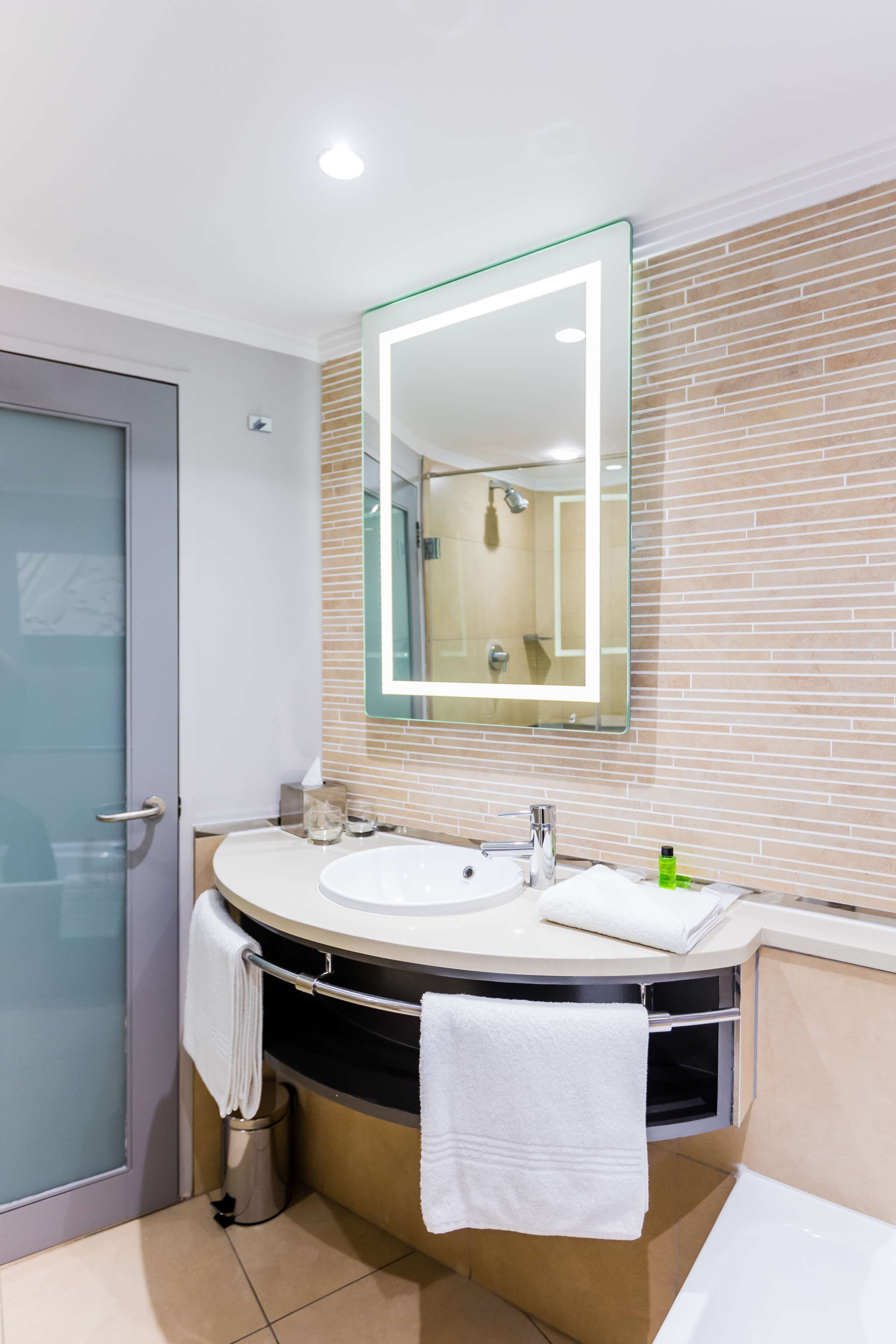 A modern bathroom with a glass shower enclosure, a white sink, and a large mirror with a lighted frame.