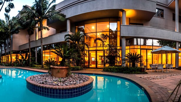 Un hotel moderno con piscina, palmeras y mobiliario de exterior.