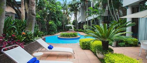 A poolside area with lounge chairs, a small pool, and lush greenery.
