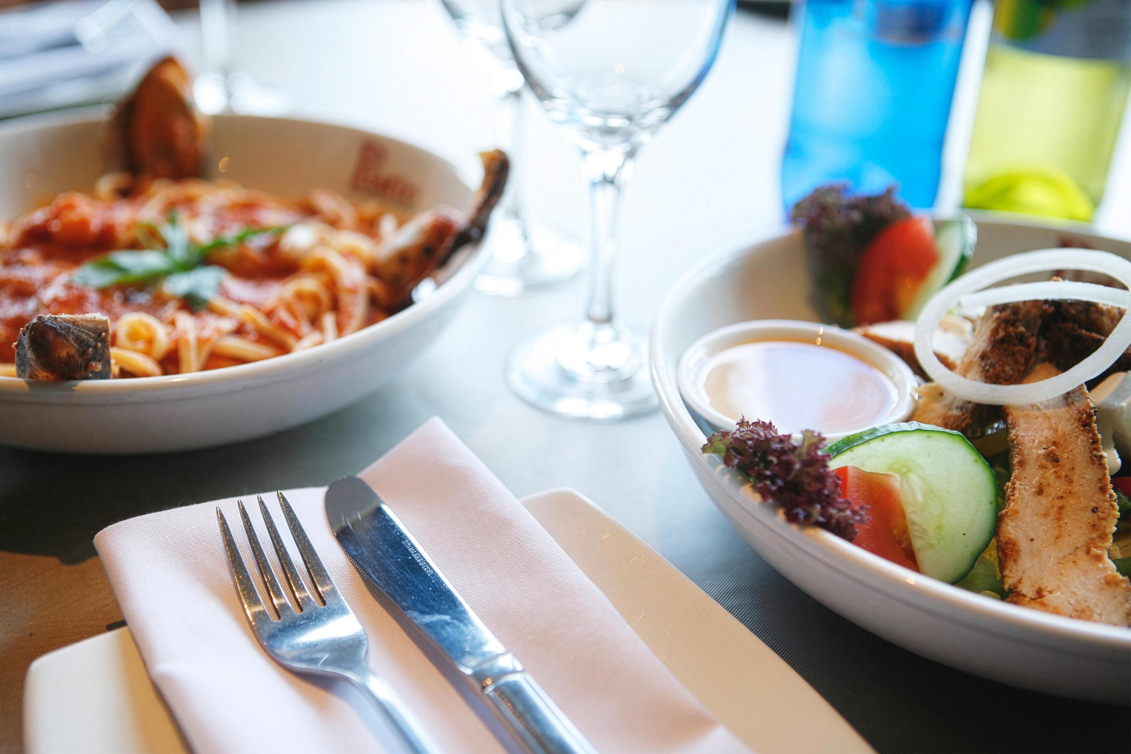 A dining table with a plate of pasta, a salad, and a glass of water.