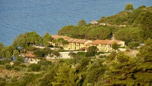 Un hôtel en bord de mer, composé de plusieurs bâtiments, entouré d’une végétation luxuriante et offrant une vue sur la mer.