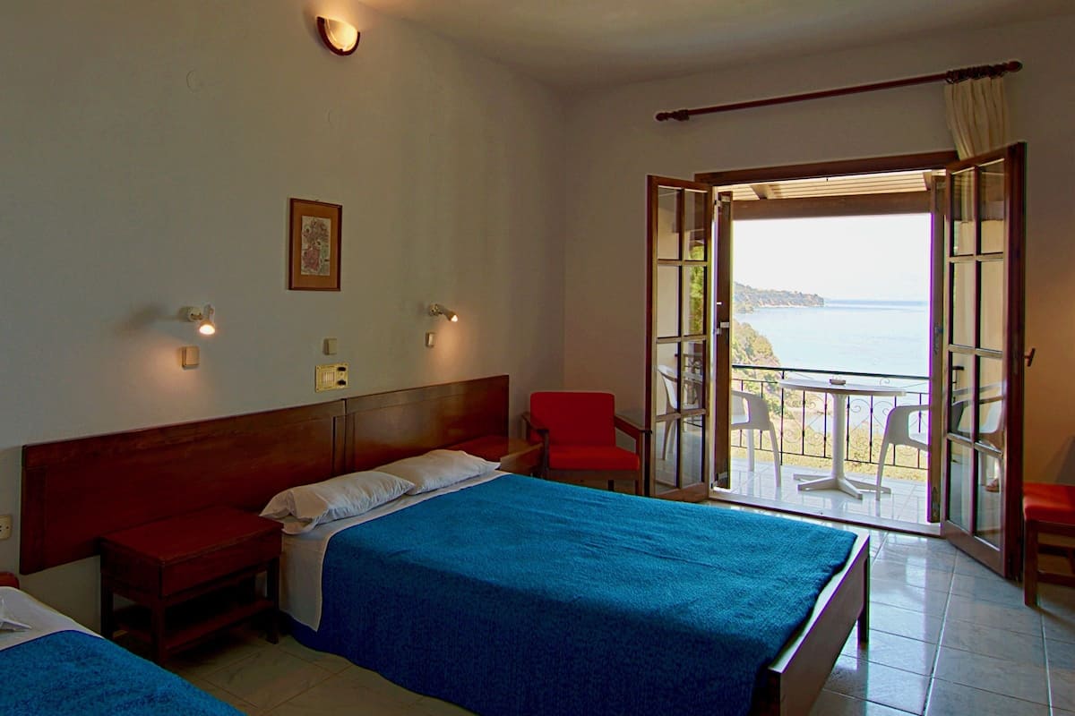 A hotel room with two beds, a balcony with a table and chairs, and a view of the sea.