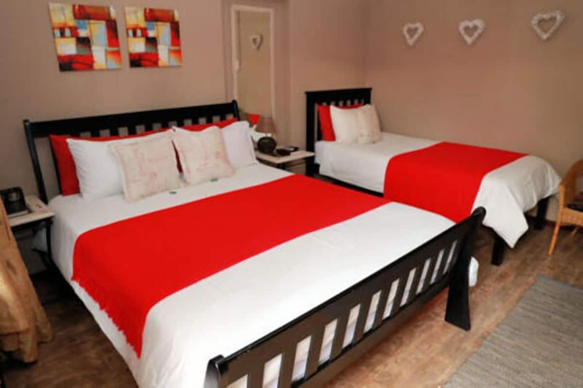 Une chambre d’hôtel avec deux lits, chacun recouvert d’une courtepointe rouge et blanche, doté d’une tête de lit en bois et agrémenté d’une table de chevet avec une lampe.