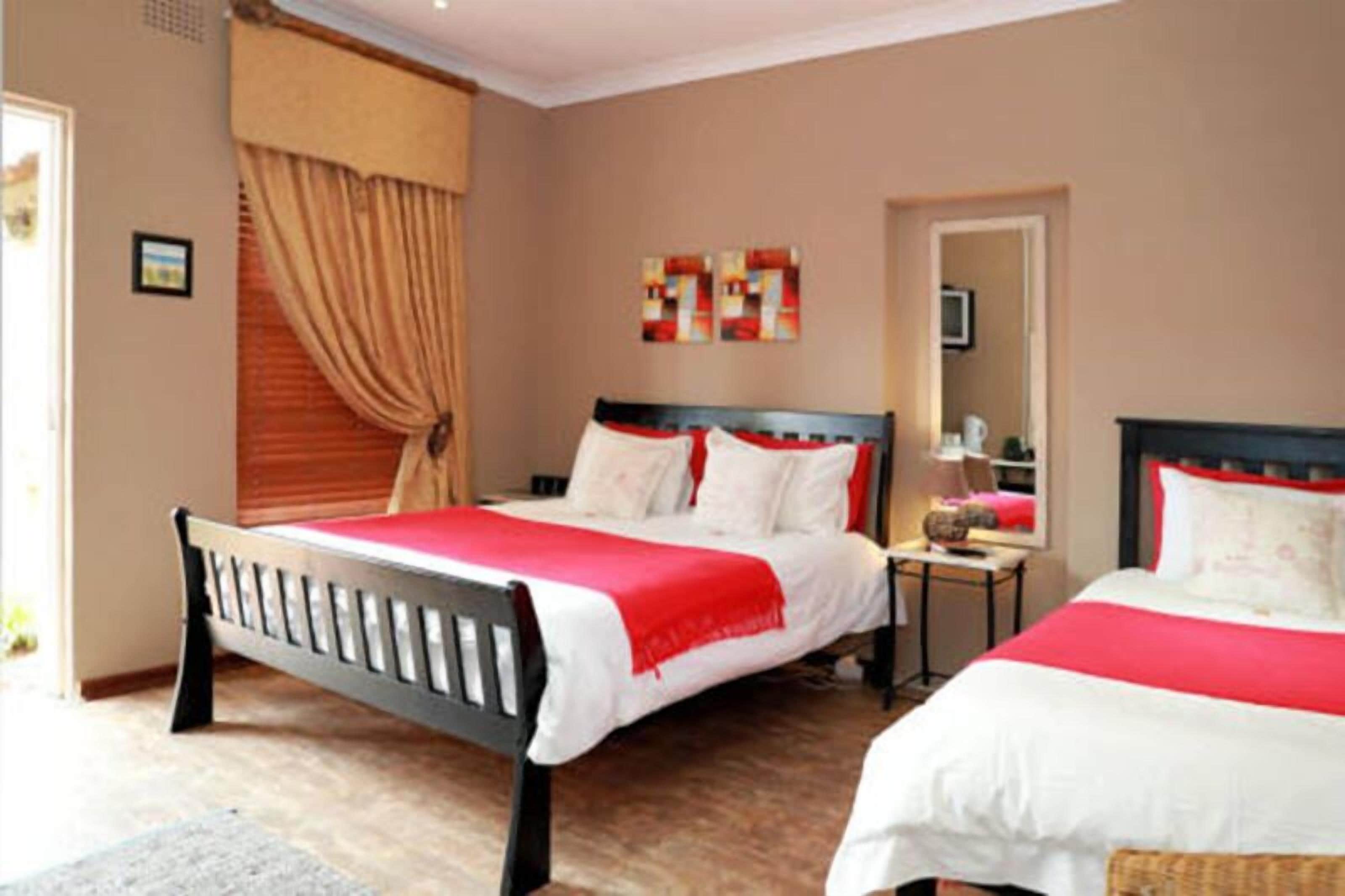 A bedroom with two beds, a nightstand, a mirror, and a window with curtains.